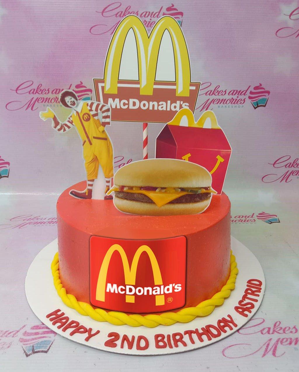 Red McDonald's themed birthday cake with Ronald McDonald, Happy Meal, and burger printout toppers on a yellow rope border base.