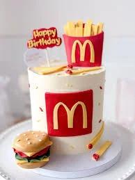 McDonald's themed birthday cake with a fondant burger, fries, and the iconic golden arches logo on a white icing base.