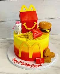 McDonald's themed birthday cake with 3D fondant Happy Meal box, burger, fries, and nuggets on a yellow and red gradient icing base.