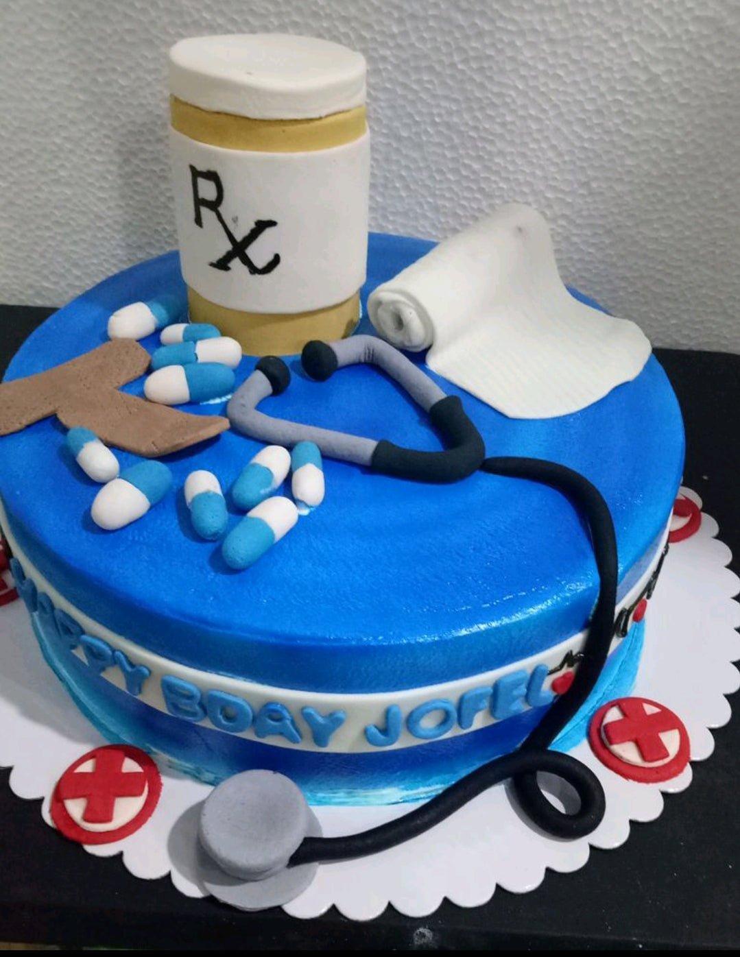 Blue medical themed birthday cake with fondant stethoscope, medicine bottle, pills, and bandage decorations.