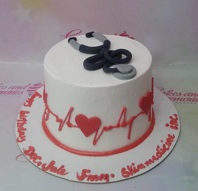 White medical themed cake with a black fondant stethoscope on top and red heartbeat line with hearts on the side.