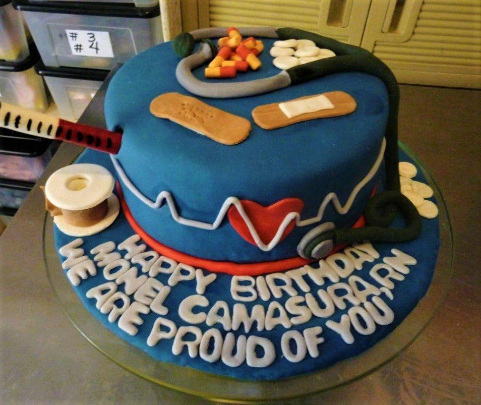 Blue fondant medical themed birthday cake with stethoscope, syringe, bandages, and pills decorations.