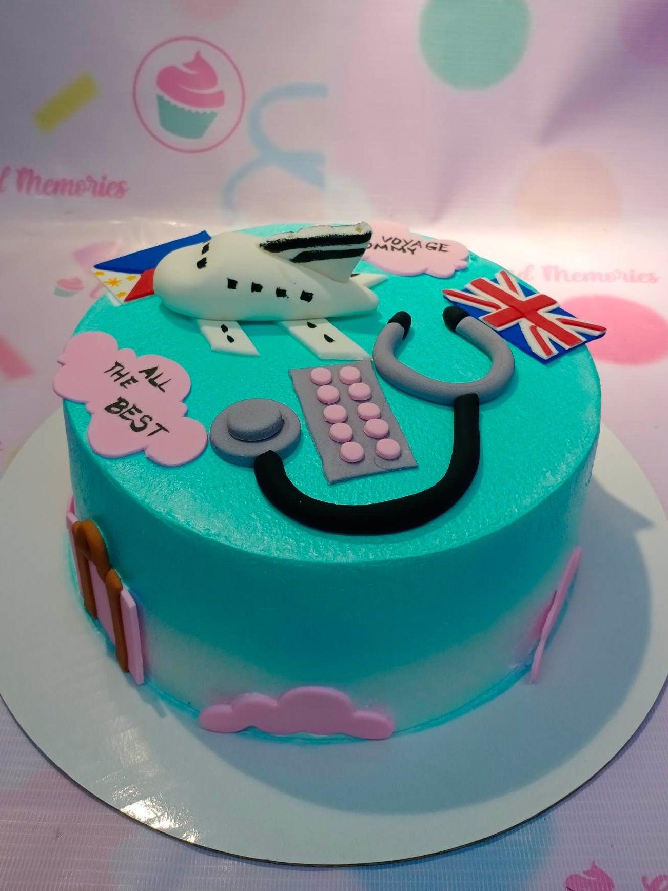 Teal and white gradient cake with fondant airplane, stethoscope, medicine, and flags for a travel and medical themed celebration.