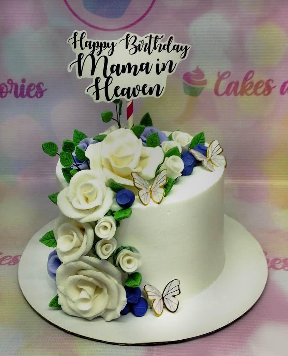 White minimalist cake with cascading white and purple gumpaste roses, green leaves, and gold-trimmed butterflies for a memorial birthday.