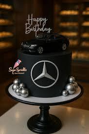 Black Mercedes Benz themed birthday cake with a toy car topper, silver logo, and silver decorative balls.