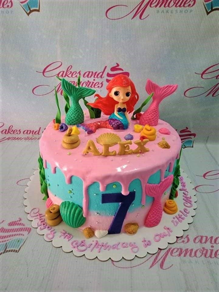 Mermaid themed birthday cake with a 3D Ariel figure, pink drip icing, and fondant sea elements like tails and shells.