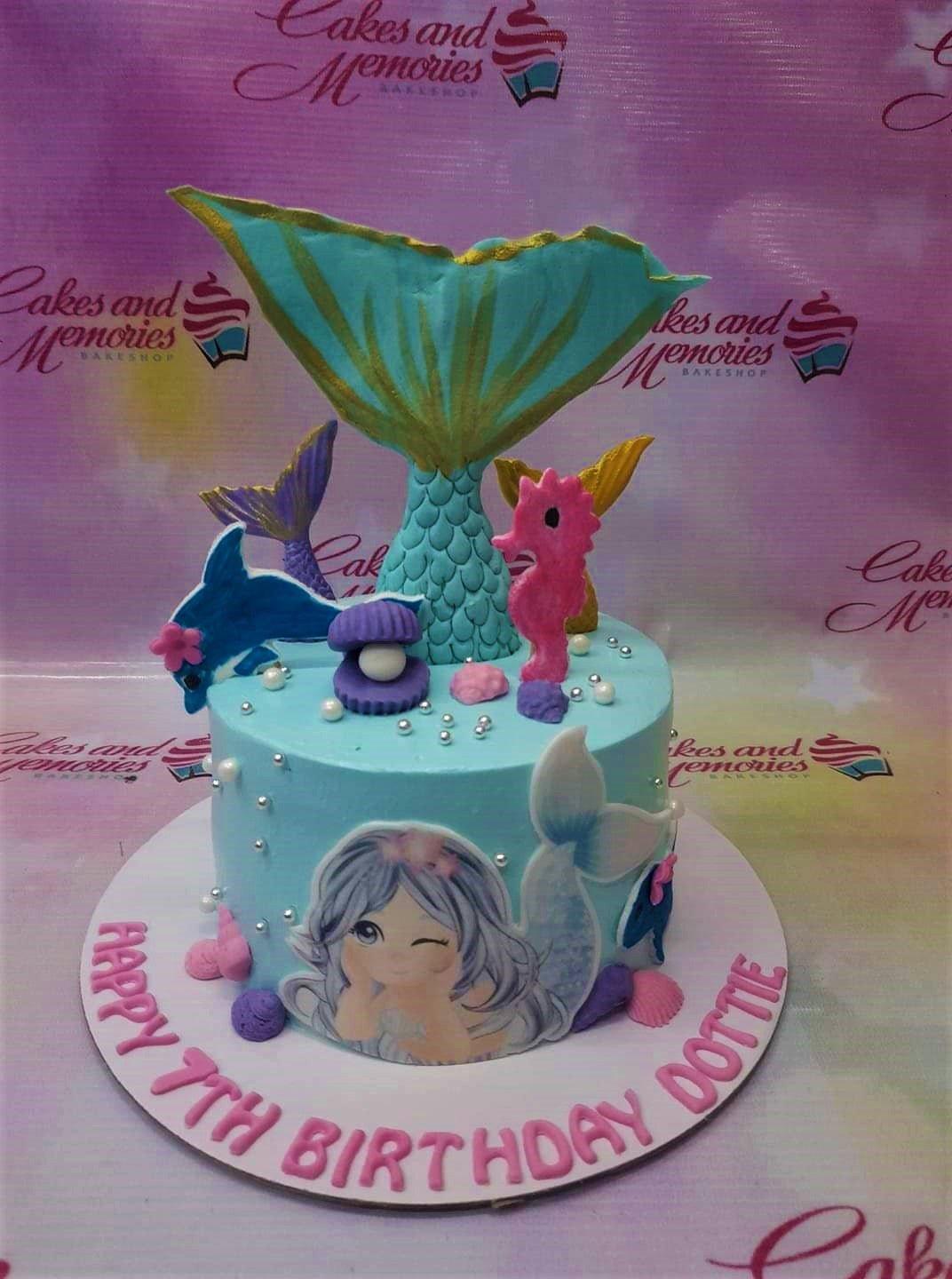 Light blue mermaid themed birthday cake with a large teal mermaid tail, pink seahorse, and edible mermaid printout.
