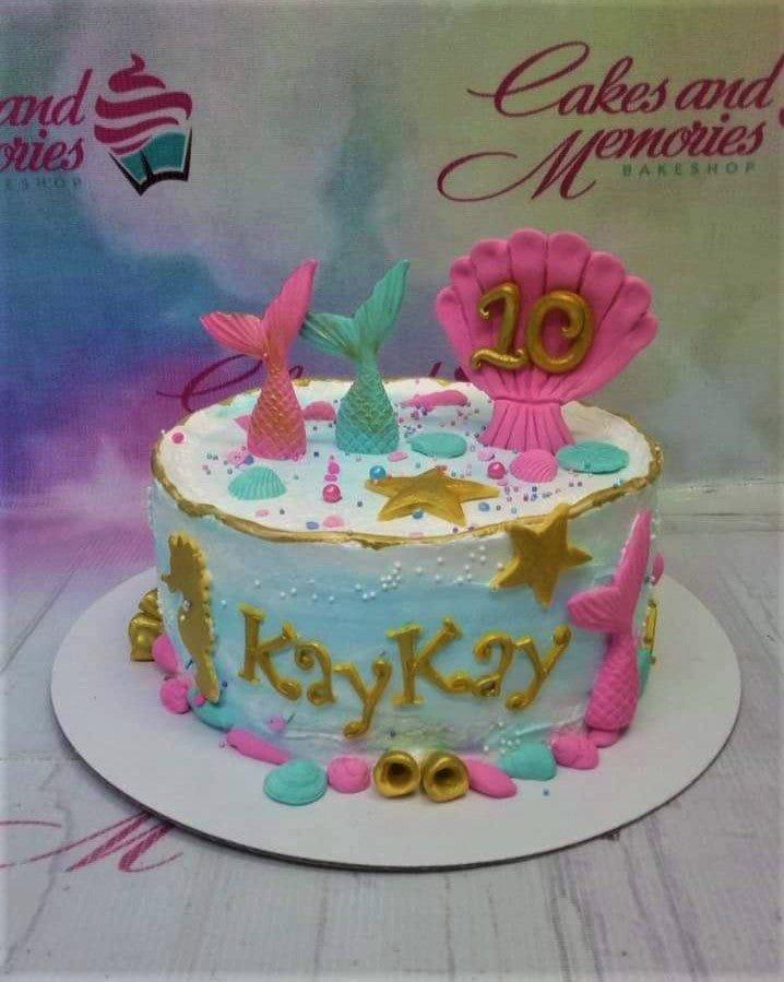Under the sea themed birthday cake with pink and teal mermaid tails, a large pink shell with gold number 10, and gold stars.