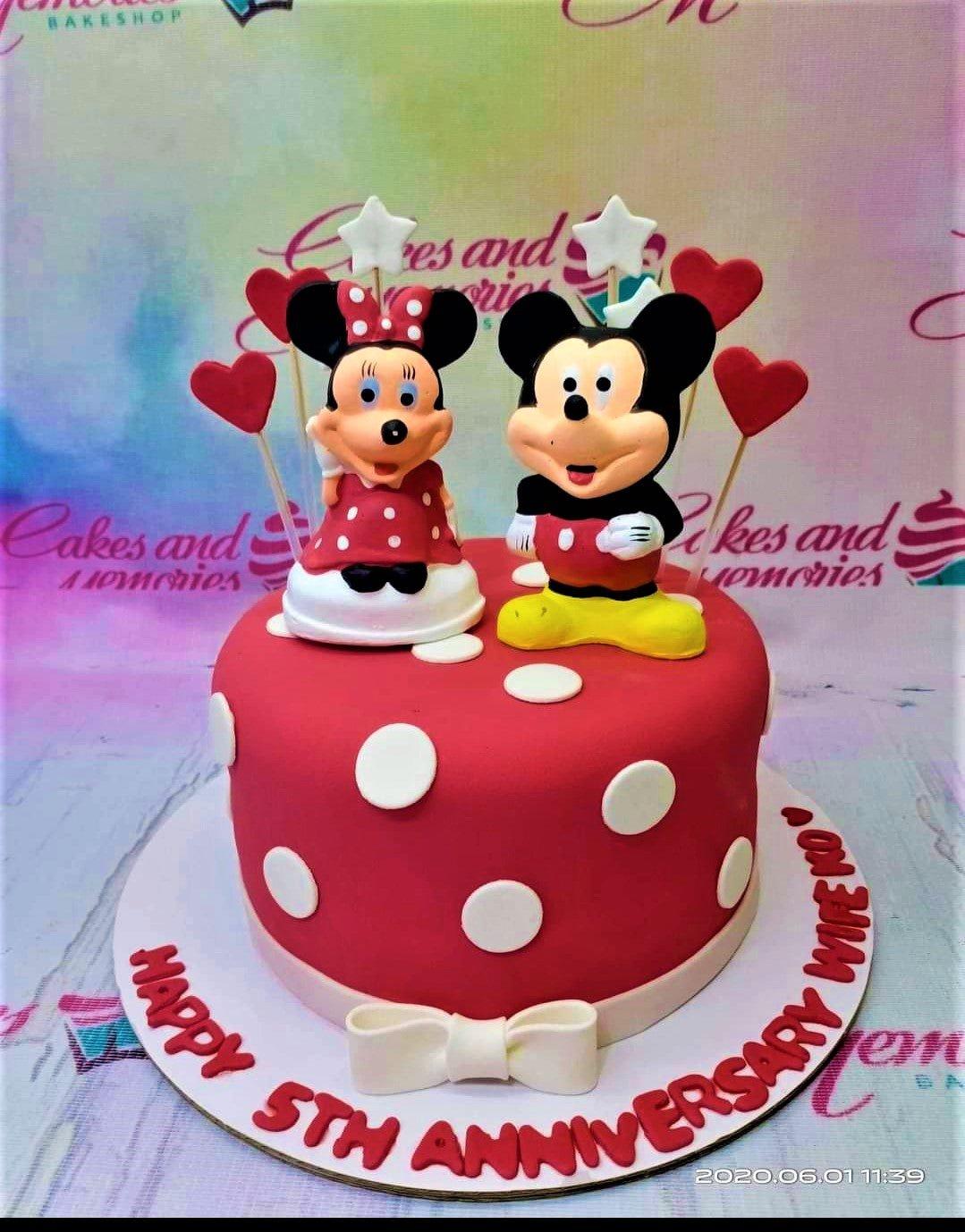 Red fondant anniversary cake with white polka dots featuring 3D Mickey and Minnie Mouse figures and red heart toppers.