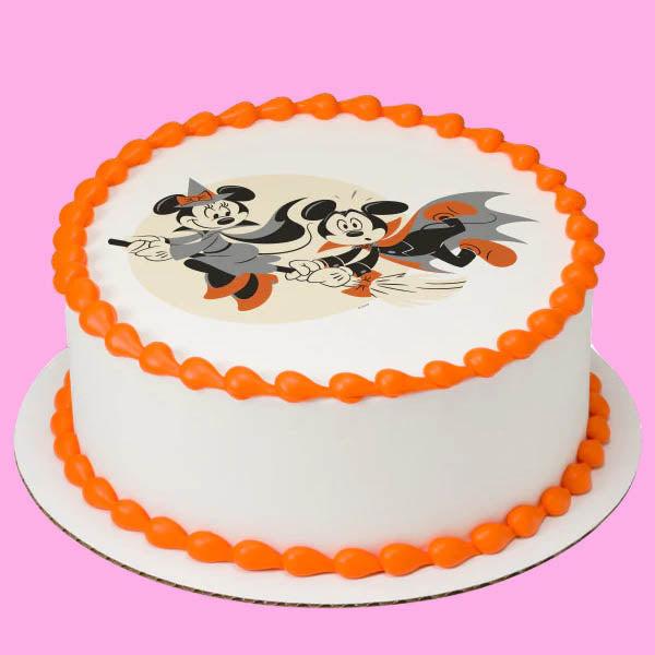 White round cake with orange piped borders and a printed Mickey and Minnie Mouse Halloween design on top.
