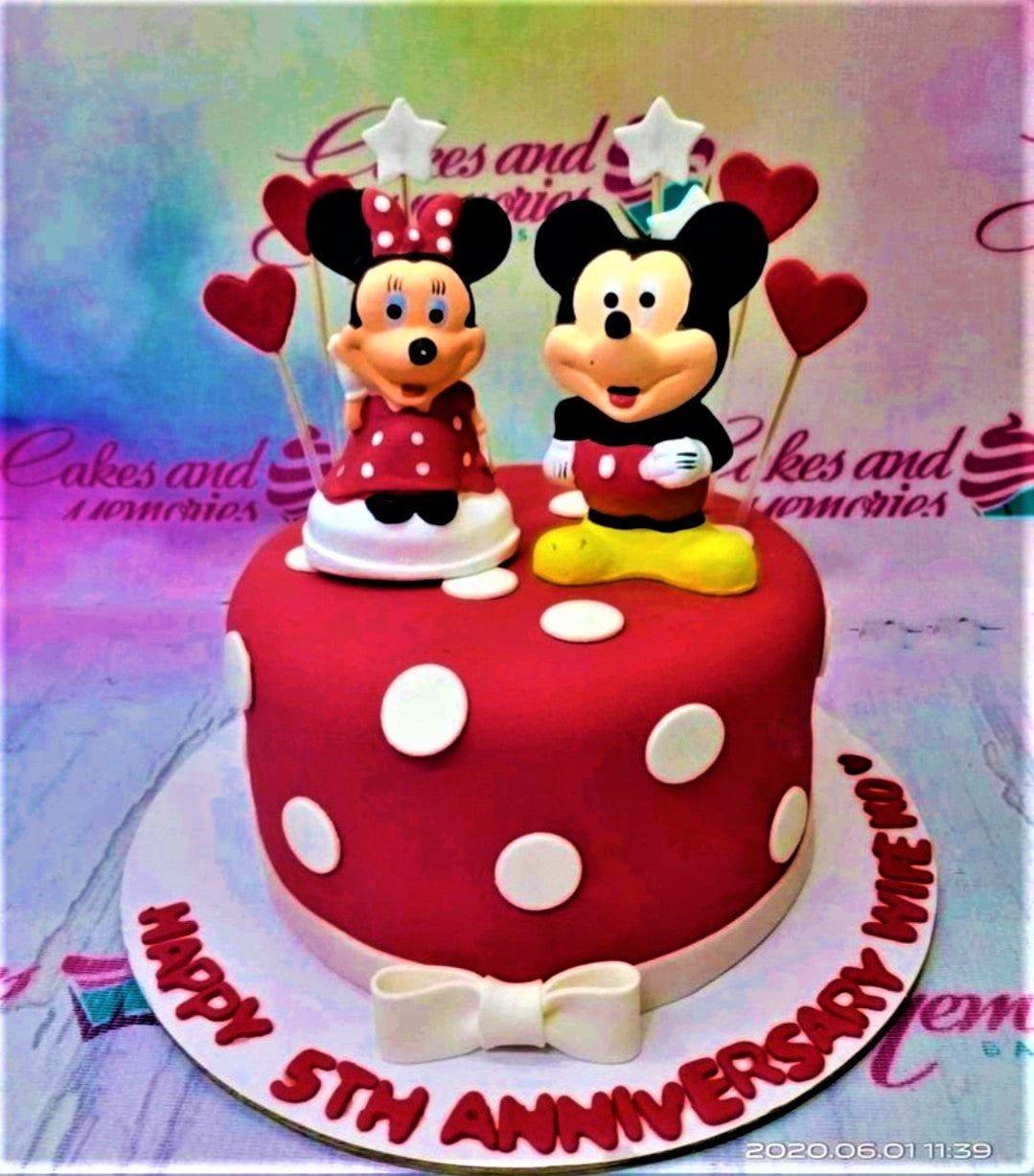 Red fondant anniversary cake with white polka dots featuring Mickey and Minnie Mouse fondant figures and red heart toppers.