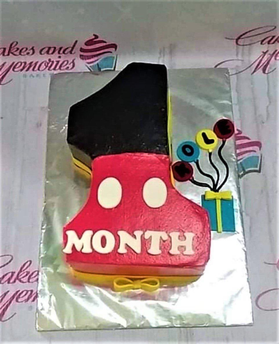 Mickey Mouse themed number one shaped cake in red, black, and yellow with a gift box and balloon printouts.
