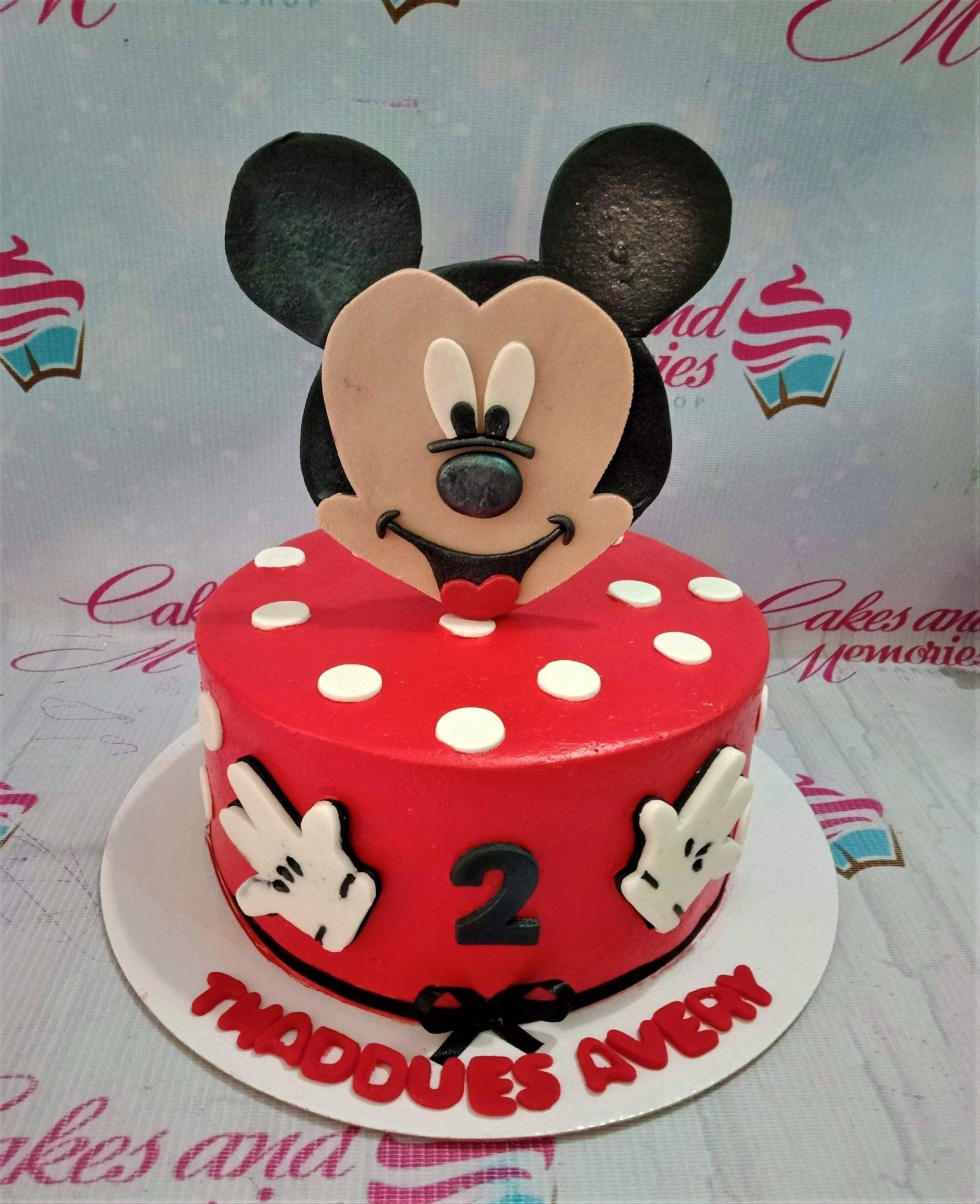 Red Mickey Mouse themed birthday cake with white polka dots, fondant Mickey face topper, and white glove decorations.