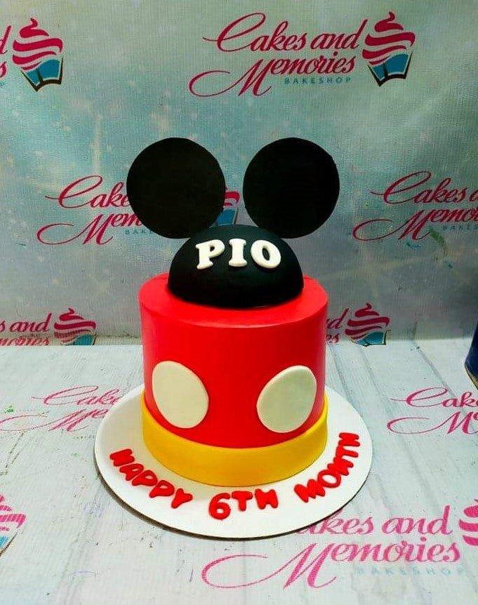 Mickey Mouse themed red and yellow fondant cake with black ears and white button accents for a 6th month celebration.