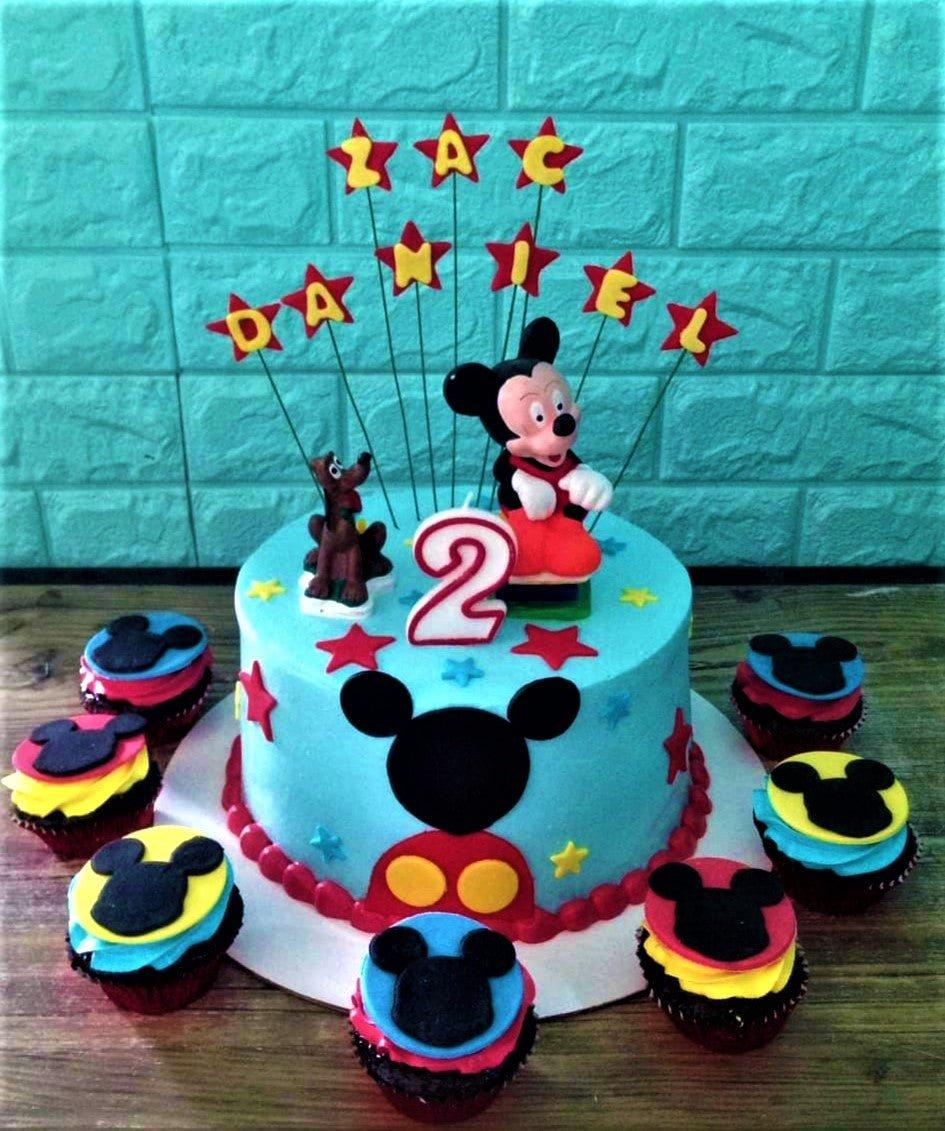 Light blue Mickey Mouse themed birthday cake with red stars, a number 2 candle, and a Mickey Mouse figurine on top.