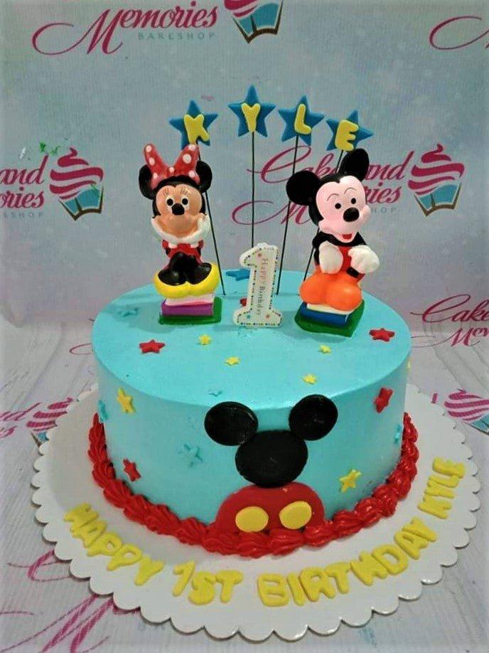 Light blue Mickey and Minnie Mouse themed birthday cake with 3D figures, stars, and red icing border.