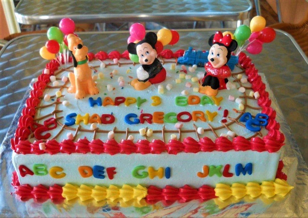 Light blue rectangular Mickey and Minnie Mouse birthday cake with red and yellow icing borders and colorful alphabet letters.