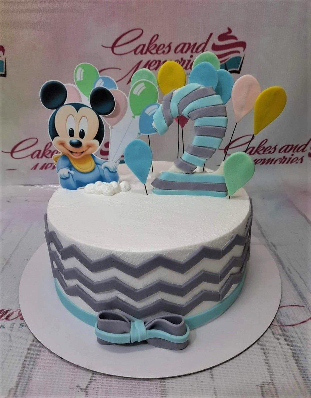 White 1-tier Mickey Mouse birthday cake with blue and gray chevron patterns, a large striped number 2, and colorful balloon toppers.