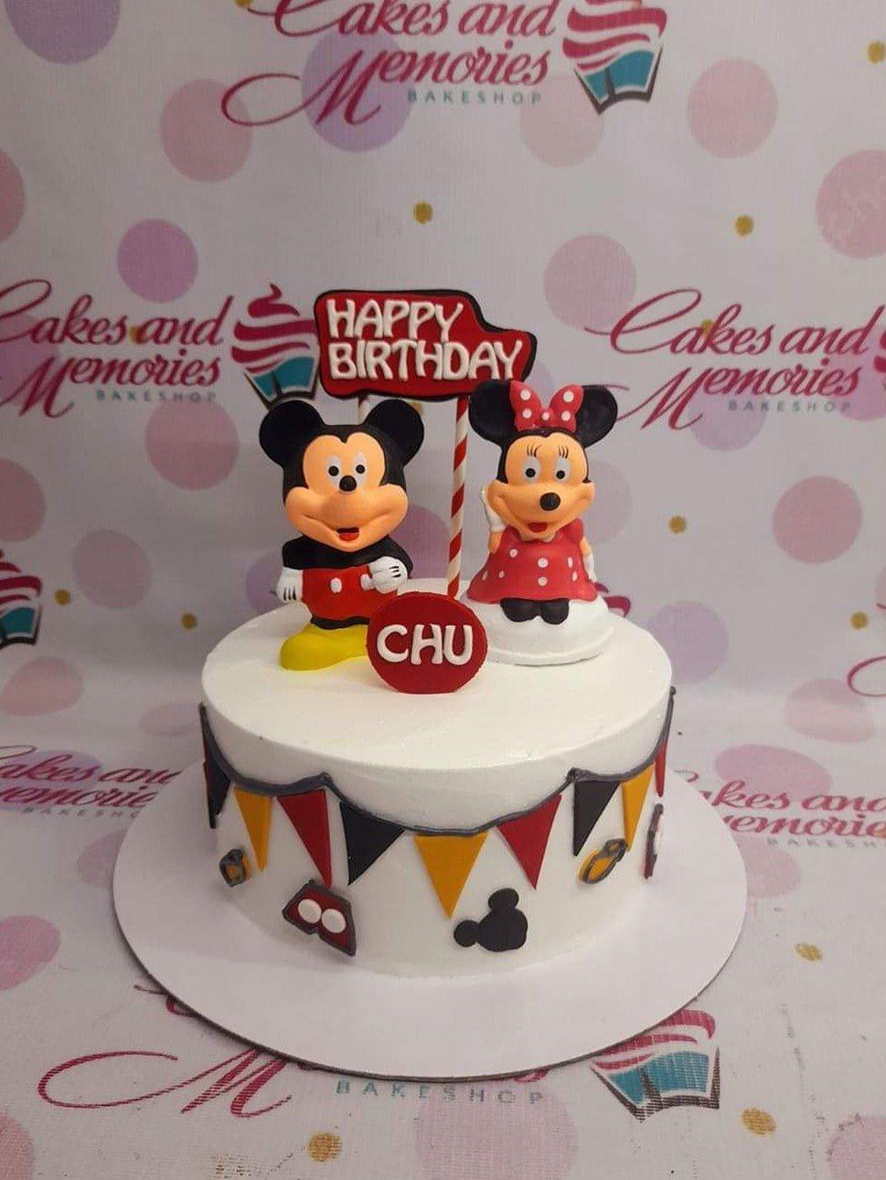 Mickey and Minnie Mouse themed birthday cake with red and black bunting and character toppers.