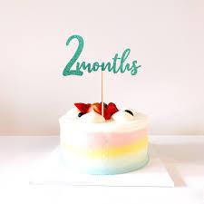 A minimalist 1-tier cake with pastel gradient icing in pink, yellow, and blue, topped with fresh strawberries and a teal 2 months topper.