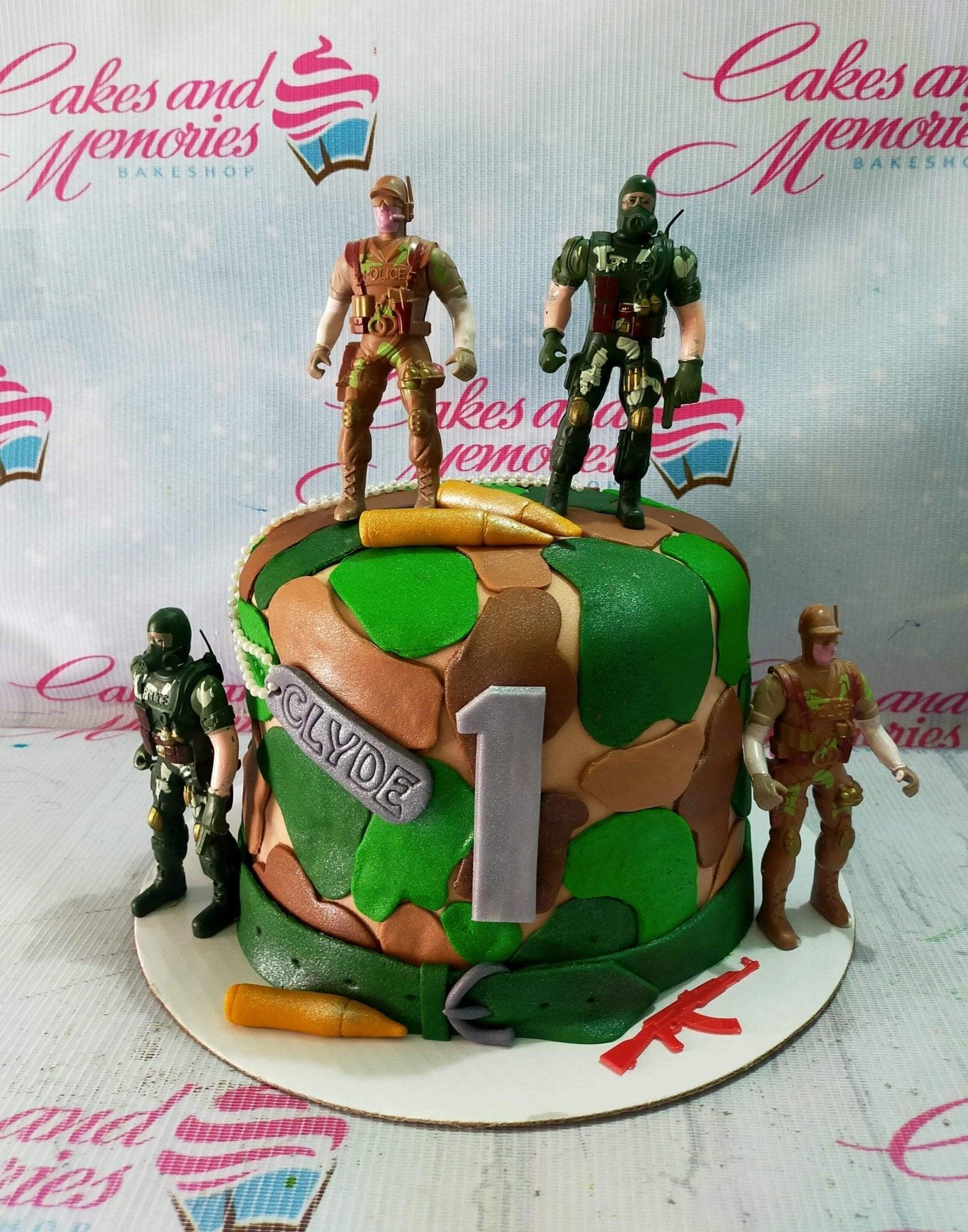 Military camouflage fondant cake with soldier action figures, bullets, and a silver number one topper for a first birthday.