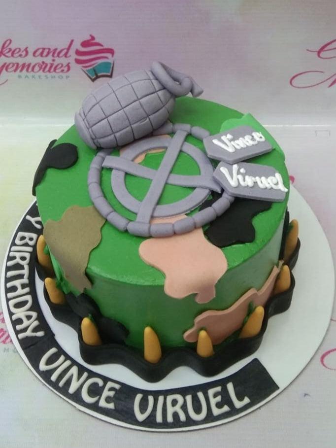 Military camouflage themed birthday cake with a 3D fondant grenade, dog tags, and bullet accents on a green base.