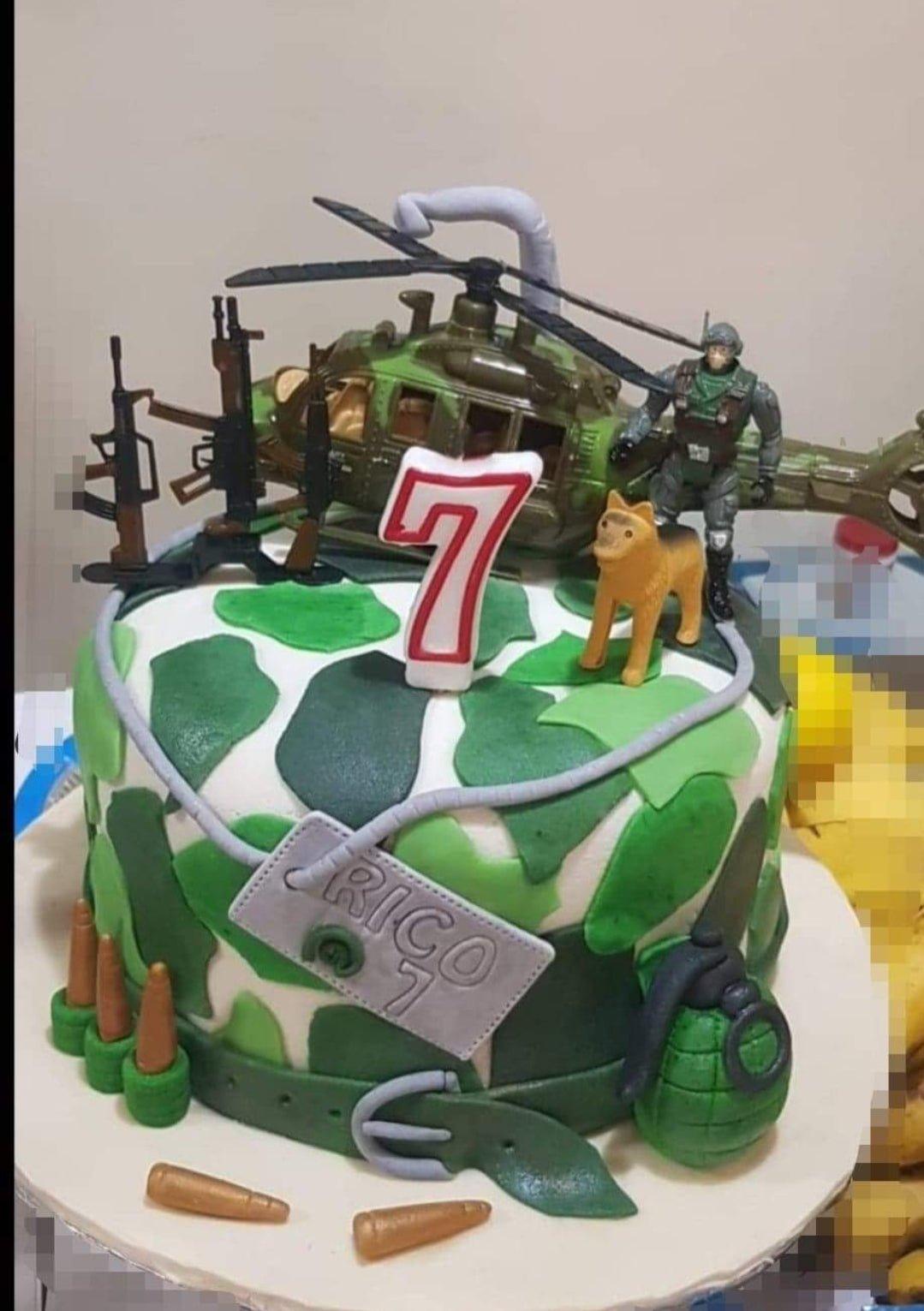Military camouflage themed cake with a toy helicopter, soldier, and fondant grenades and bullets.