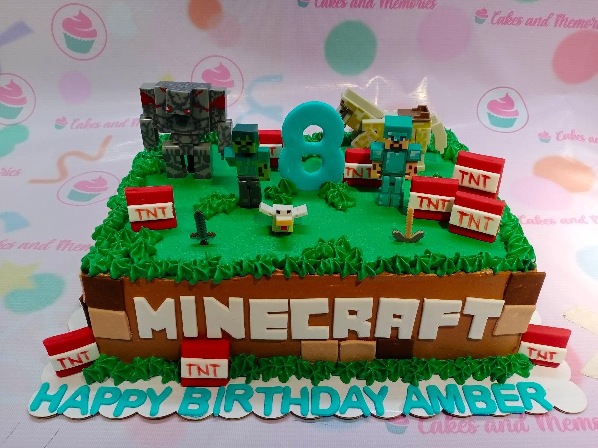 Minecraft themed rectangle cake with green grass icing, brown sides, TNT blocks, and character figurines including Steve and a Creeper.