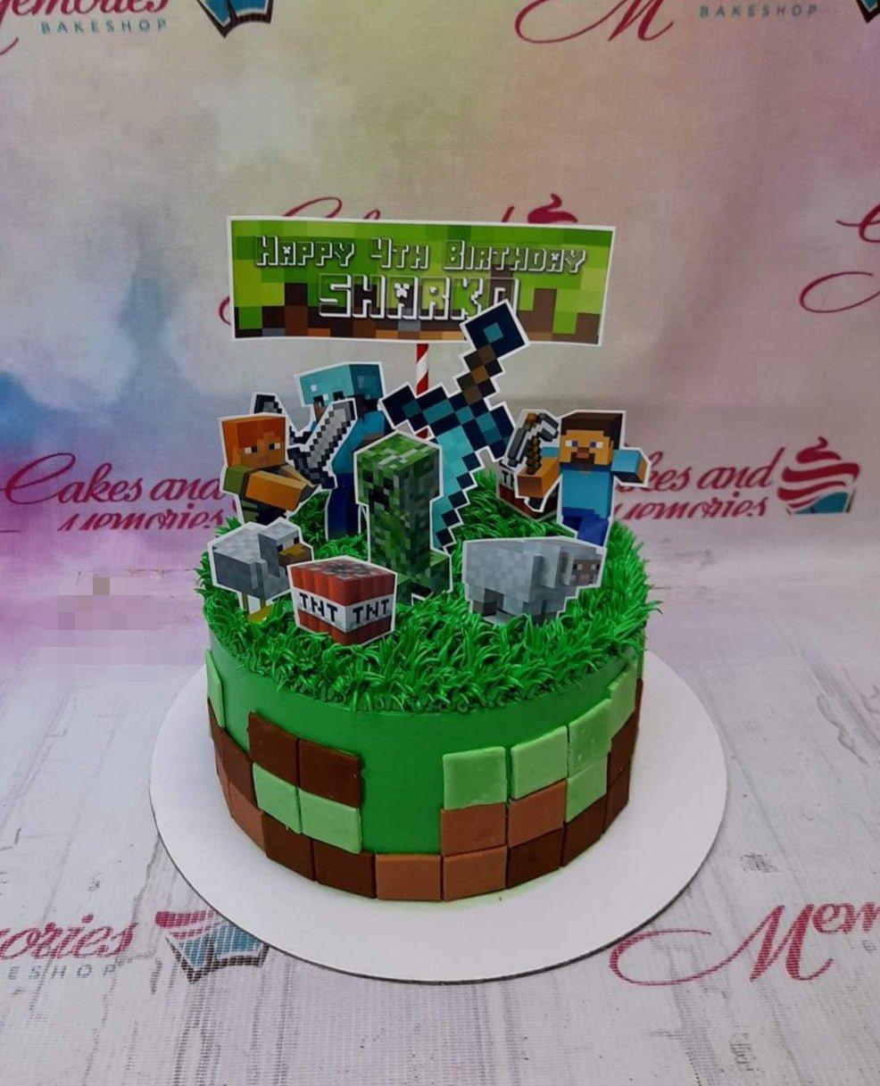 Minecraft themed birthday cake with green grass icing, brown and green pixel blocks, and character printouts for a 4th birthday.