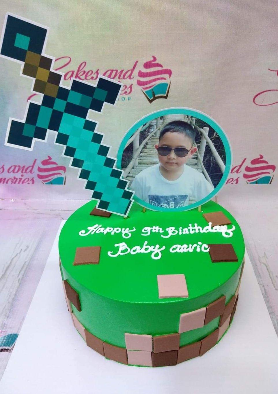 Green Minecraft themed birthday cake with a pixelated sword topper, a photo printout of a boy, and brown and tan square fondant accents.