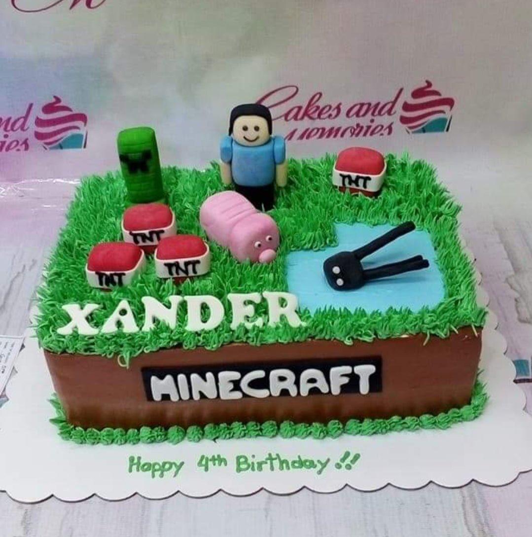 Minecraft themed rectangle cake with green grass icing, fondant TNT blocks, a creeper, a pig, and a Steve character figure.
