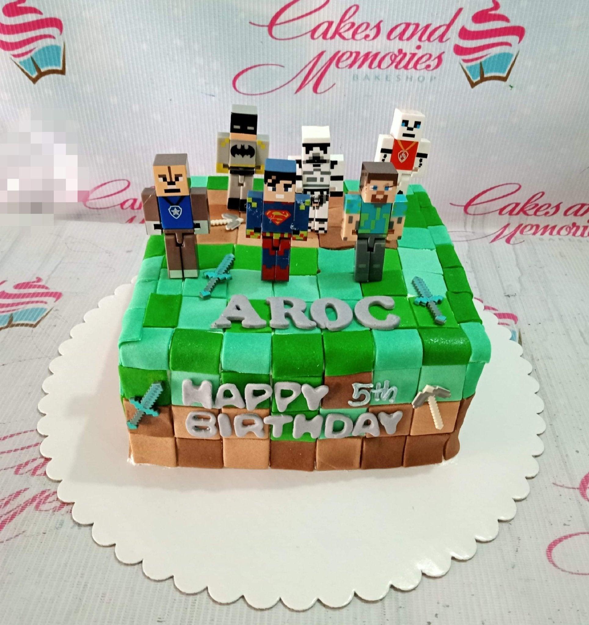 Minecraft and superhero themed square fondant cake with pixelated green and brown blocks and 3D character figures.
