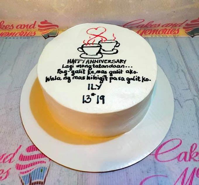 White minimalist bento cake with black and red icing illustrations of coffee cups and a heart, featuring a humorous anniversary message.