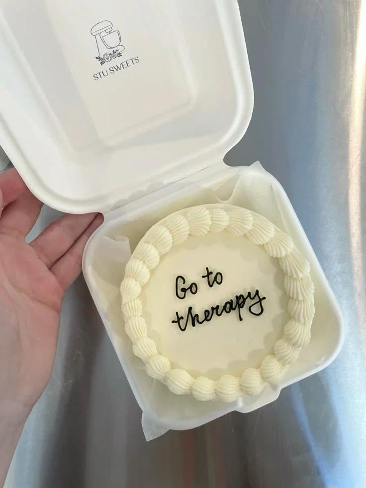 White minimalist bento cake with cream shell borders and black cursive icing text saying Go to Therapy.