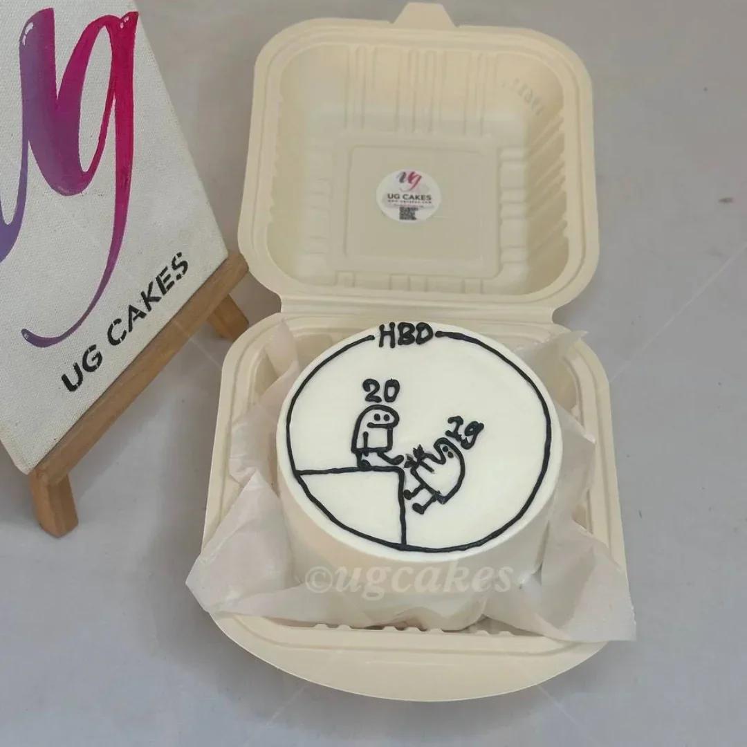 White bento cake with black minimalist icing doodle of two figures and 'HBD 20 19' message in a cream container.