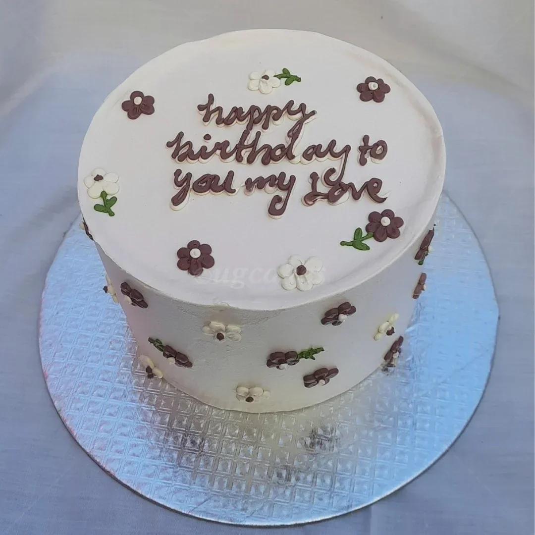 White bento cake with brown and white piped icing flowers and a handwritten birthday message in brown icing.