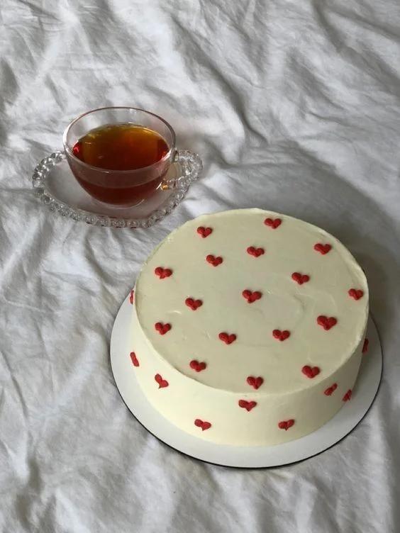Minimalist white round cake decorated with small red piped icing hearts on the top and sides.