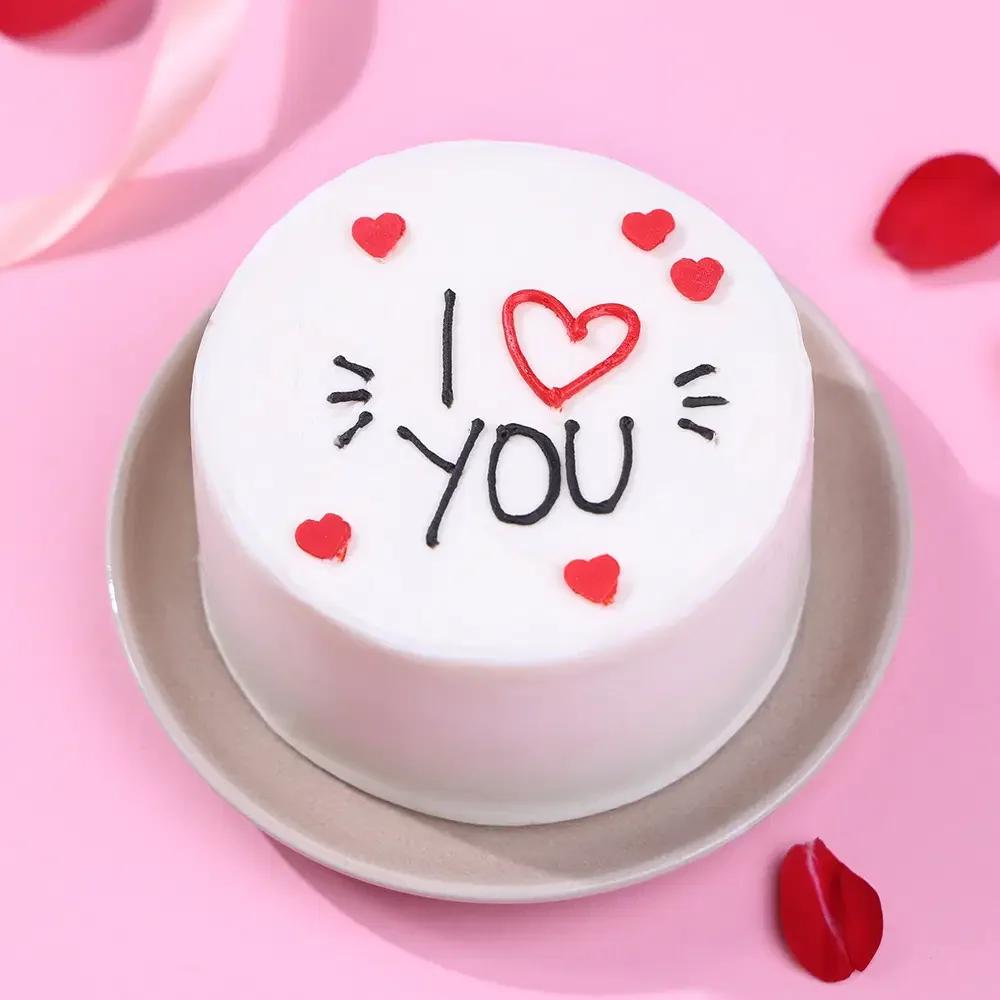 White bento cake with red icing hearts and black piped 'I YOU' message with a red heart symbol.