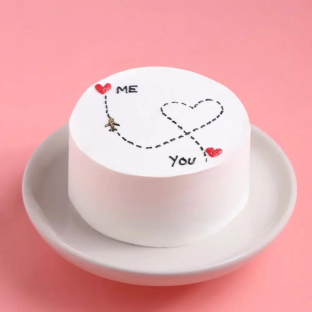 White bento cake with minimalist icing doodle of an airplane flying between 'Me' and 'You' with red hearts.