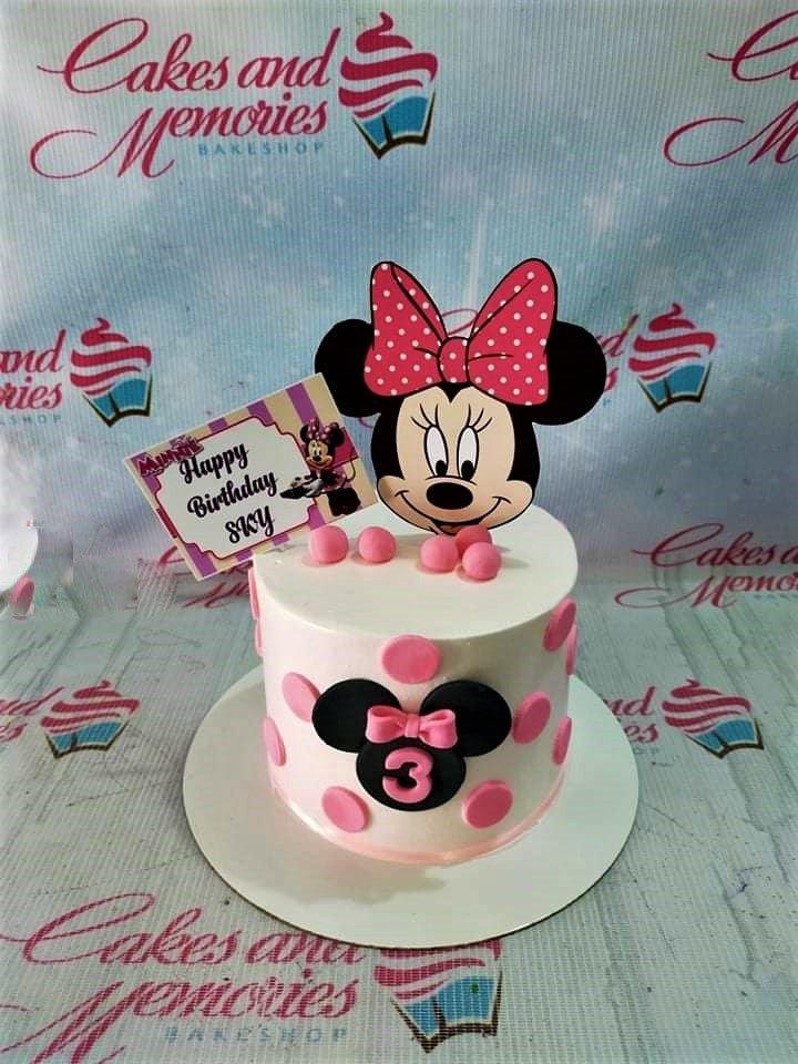 White Minnie Mouse themed birthday cake with pink polka dots and a large Minnie Mouse printout topper.