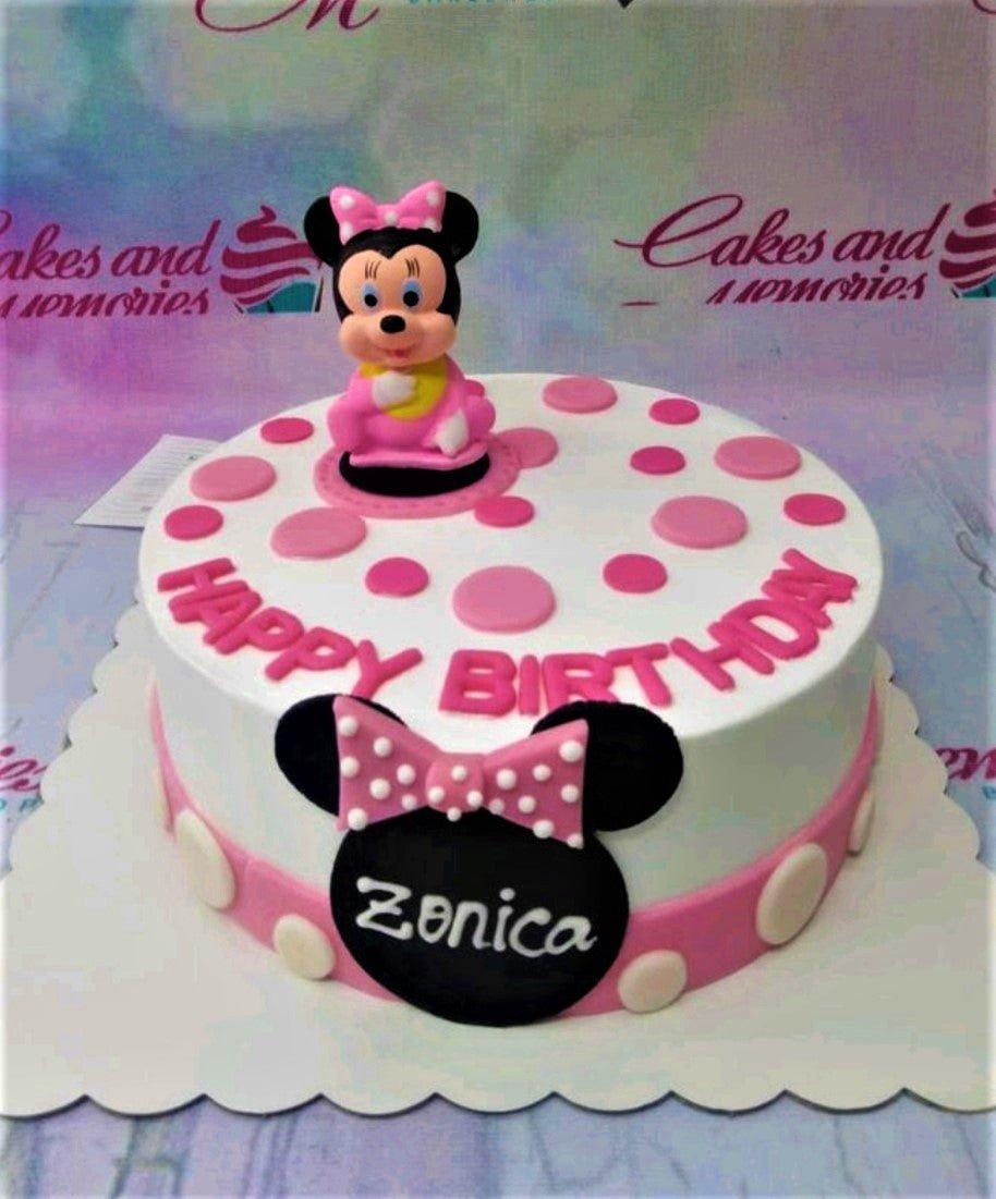 White Minnie Mouse birthday cake with pink polka dots, a 3D Minnie figurine, and a large black Minnie silhouette with the name Zonica.