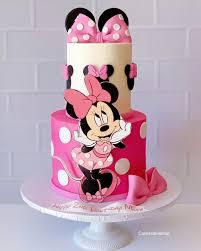 Two-tier Minnie Mouse themed cake with pink and white fondant, featuring a large Minnie Mouse cutout and pink bows.