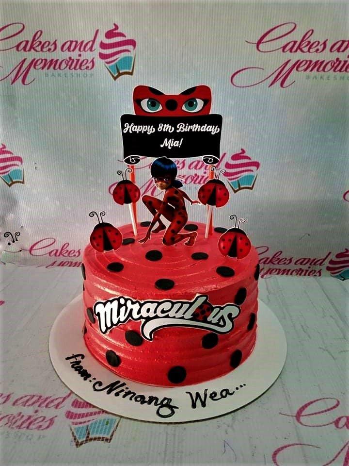 Red Miraculous Ladybug themed birthday cake with black polka dots and character printouts for Mia's 8th birthday.