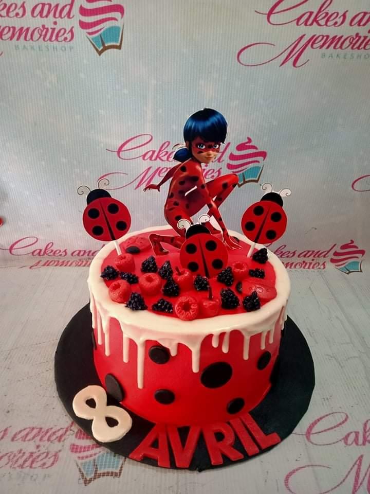 Red Miraculous Ladybug themed cake with black polka dots, white drip, and ladybug toppers.
