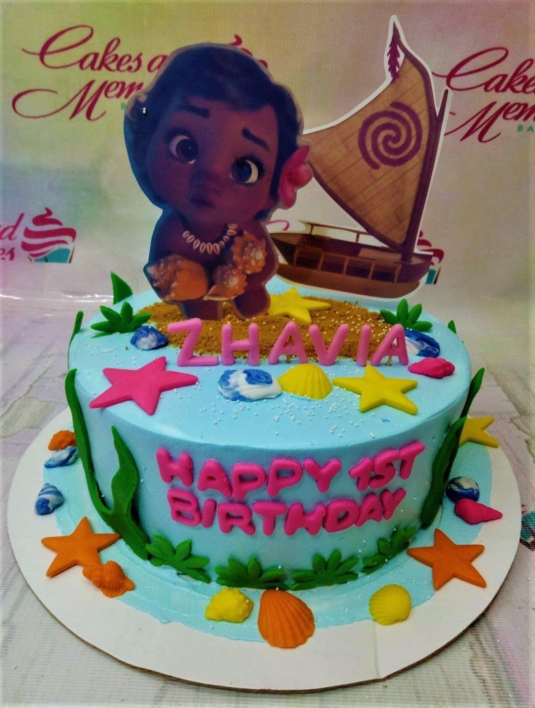 Moana themed light blue birthday cake with Moana character printouts, fondant sea shells, and pink gumpaste letters.