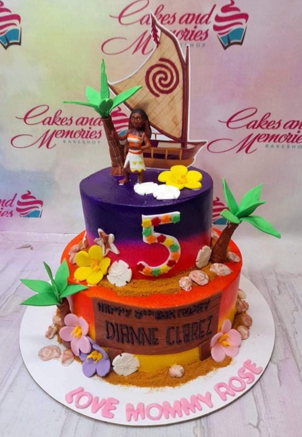 Moana themed 2-tier birthday cake with sunset gradient icing, palm trees, Moana figurine, and a large sailboat topper.