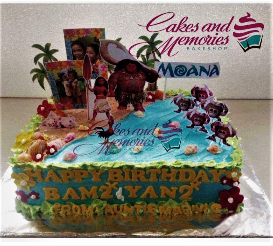 Moana themed rectangle cake with blue icing water, sand texture, and character printouts of Moana, Maui, and Kakamora.