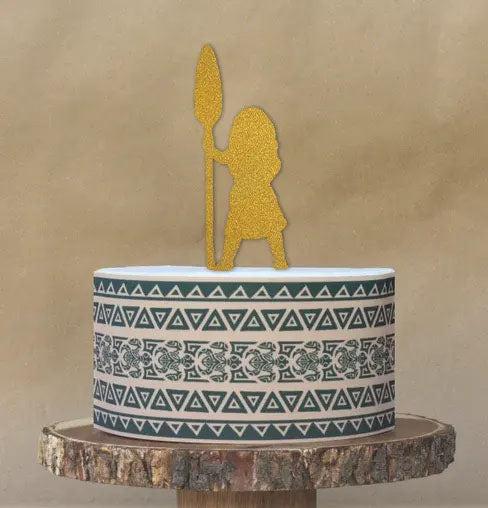 Moana themed birthday cake with a gold glitter silhouette topper and tribal pattern side wrap on a rustic wood stand.