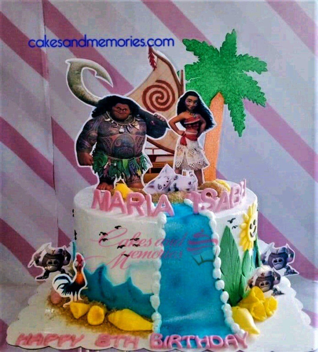 Moana themed birthday cake with Maui, Moana, and Hei Hei printouts, a blue icing waterfall, and yellow gumpaste shells.