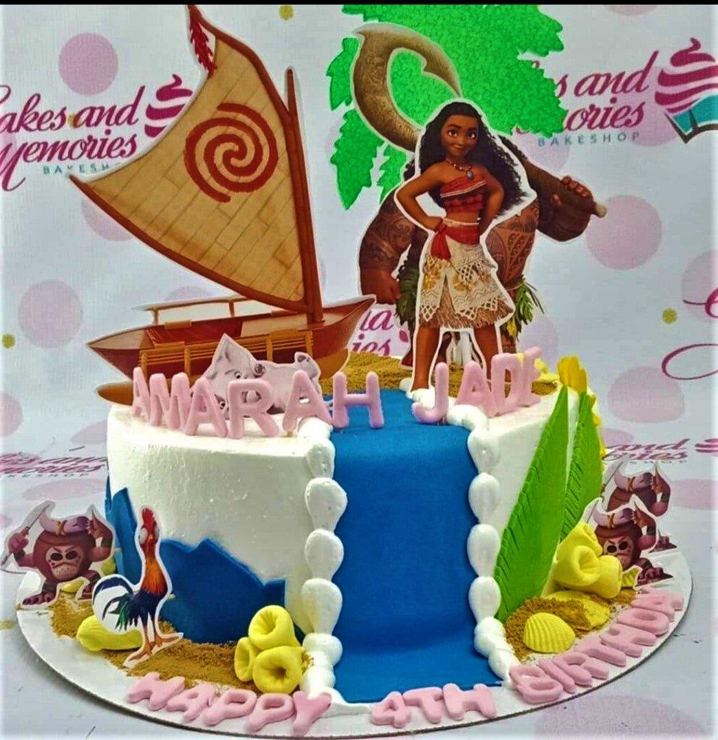 Moana themed birthday cake with a blue waterfall, Moana and Maui printouts, and pink gumpaste letters on a white icing base.